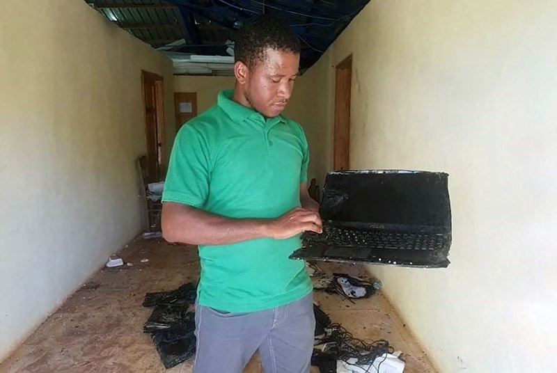 Mario Damis, coordinador de HAPITech, el centro de capacitación vocacional de Haitian Assets for Peace International, inspecciona una pila de 15 computadoras portátiles destruidas después de que el almacén se quemó en la madrugada del 6 de julio. Ahora su prioridad es restaurar el Internet de HAPI para ayudar a restablecer las comunicaciones tan necesarias, en este tiempo turbulento que vive Haití. Foto cortesía de Valerie Mossman-Celestin
