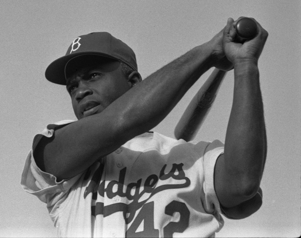 Baseball great Jackie Robinson swings a bat in his Dodgers uniform, dated 1954. This photo was taken by a staff photographer of LOOK Magazine and is part of the LOOK Magazine Photograph Collection at the Library of Congress, courtesy of Wikimedia Commons.