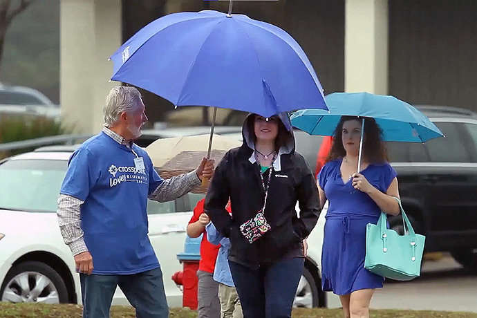 A volunteer holds an umbrella for a woman at Crosspoint, a United Methodist church in Niceville, Fla. Ninety percent of the congregation at its South Crestview campus volunteers in some capacity. Video image courtesy of Crosspoint via Vimeo by UM News.