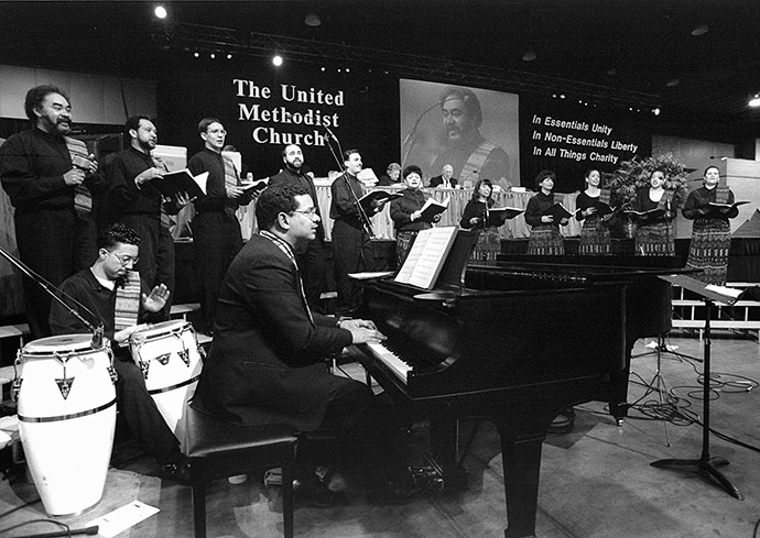 Jorge Lockward toca el piano y dirige la Coral Metodista Unida Hispana de Nueva York mientras delegados/as y visitantes, a la Conferencia General Metodista Unida de 1996 en Denver, cantan con el himnario "Mil Voces Para Celebrar". Foto de archivo de Mike DuBose, Noticias MU.