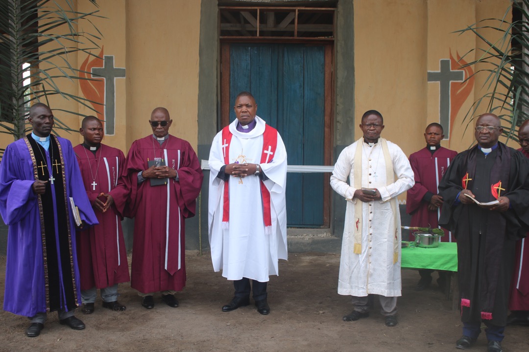 L’Evêque Méthodiste Unie Daniel Lunge entouré quelques Pasteurs du District Ecclesiastique de Djalo se tient devant le nouvelle église construite. L’église locale de Djalo a été construite grâce aux contributions des délégués de la Conférence Annuelle du Congo Central. Photo de François Omanyondo, UM News.