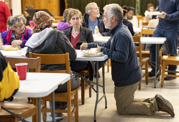 Pastor Tim Jackson kneels on the floor while joining community members for the regular Sunday evening meal at Magnolia Avenue United Methodist Church. Photo by Mike DuBose, UM News.