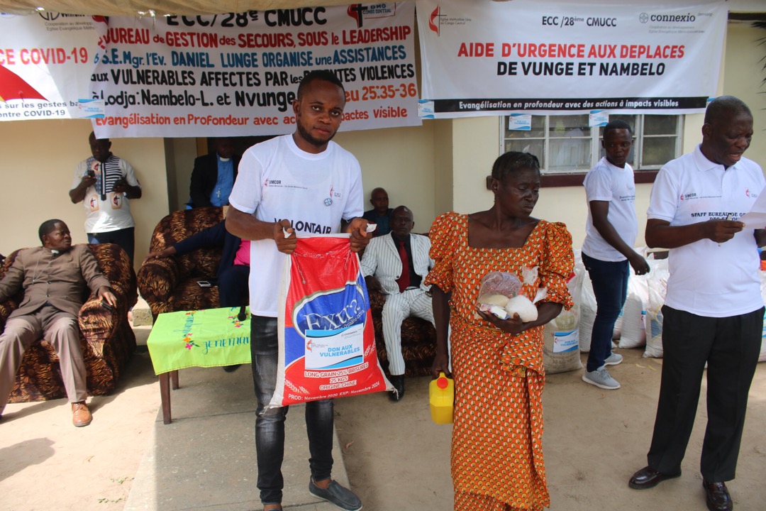 Maman Émilienne Osombo assisté du volontaire Rémy Alomba reçoit les vivres et le non vivres.  A côté c'est Mr. Émile Odimba détenant la liste des bénéficiaires lors du lancement officiel de la distribution d'aide humanitaire aux victimes. Photo par François Omanyondo, UM News.