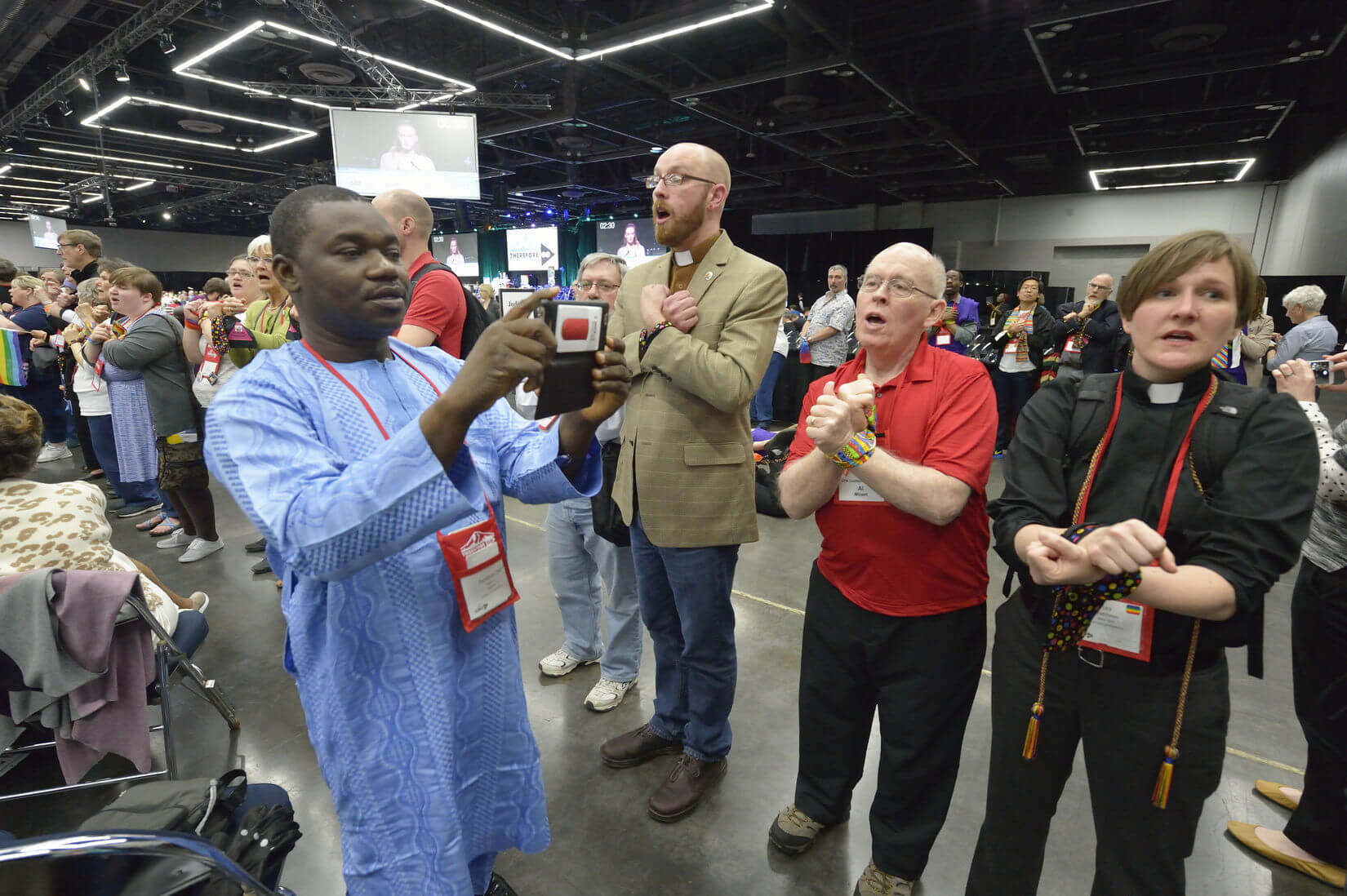 Un observateur Africain utilise son téléphone portable pour filmer des manifestants qui ont les mains liées en signe de protestation contre les politiques de la dénomination sur la sexualité humaine pendant leur démonstration du 17 Mai à la Conférence Générale de l’Eglise Méthodiste Unie à Portland (Oregon-Etats-Unis). Photo de Paul Jeffrey, UMNS