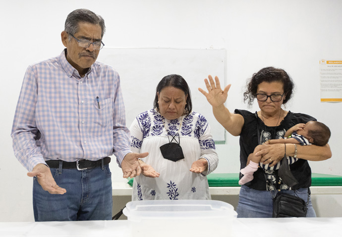 The Rev. Toña Rios cradles Dina during an impromptu baptism service at the Hospitalidad y Solidaridad migrant shelter in Tapachula. Dina was born while her family was fleeing El Salvador. Rios is a pastor at Baldwin Park (Calif.) United Methodist Church. Sharing in the service are Bishops Felipe Ruiz Aguilar and Raquel Balbuena Osorio of the Methodist Church in Mexico. Photo by Mike DuBose, UM News.
