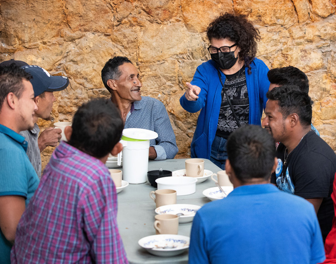 The Rev. Toña Rios of Baldwin Park (Calif.) United Methodist Church visits with migrants while they enjoy breakfast at the Oasis en el Medio del Camino migrant shelter in Apaxco, Mexico, a ministry of the Methodist Church in Mexico and the United Methodist Committee on Relief. Rios, once a migrant herself, offered prayers for the journey and advice about what to expect. Photo by Mike DuBose, UM News.