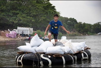 Un niño usa una balsa hecha con carcasas de llantas amarradas a tablones de madera para transportar mercancías a través del río Suchiate desde Ciudad Hidalgo en México hasta las cercanías de Ciudad Tecún Umán en Guatemala. Foto de Mike DuBose, Noticias MU.