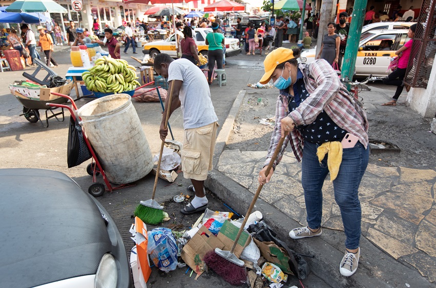 Leticia, de Honduras, y Felipé, de Haití, limpian basura de las alcantarillas en Tapachula, México. El gobierno municipal paga un pequeño estipendio a los migrantes a cambio de su trabajo bajo el  programa “Emergencia Social” el cual es una iniciativa federal del gobierno de México. Foto de Mike DuBose, Noticias MU.