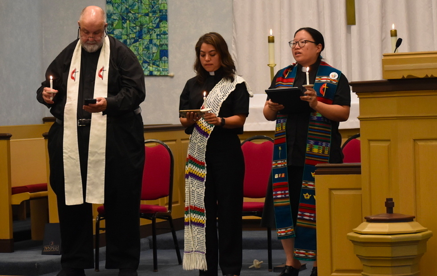 Durante una vigilia de oración el 5 de julio, el Rev. Cal Haines de Lake Bluff, la Diácona Patricia Bonilla de Grace y la Revda. Esther Lee de la IMU Cristo en Deerfield, sostienen velas y recuerdan a las víctimas y los/as heridos/as en el desfile del 4 de julio en Highland Park. Foto cortesía de la Conferencia Anual del Norte de Illinois.