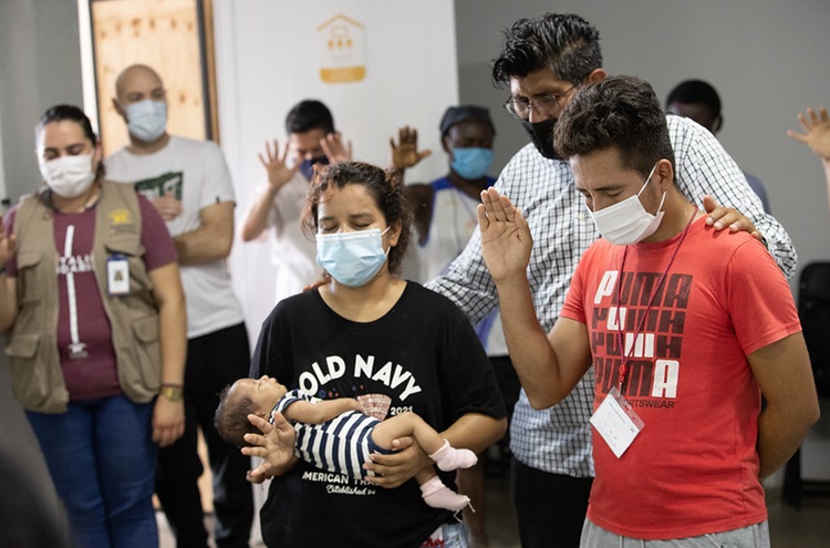 El Rev. Uzi Castañeda Morales de la Iglesia Metodista en México intercede en oración por Nancy, José y su hija Dina, luego de que la bebé fuera bautizado en el albergue Hospitalidad y Solidaridad en Tapachula. Foto de Mike DuBose, Noticias MU.