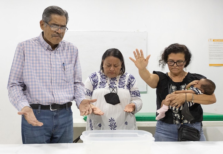 La Rvda. Toña Ríos sostiene a Dina durante un servicio de bautismo improvisado en el albergue para migrantes Hospitalidad y Solidaridad en Tapachula. Dina nació mientras su familia huía de El Salvador. Ríos es pastora de La Iglesia Metodista Unida de Baldwin Park (California). Compartiendo en el servicio están los/as obispos/as Felipe Ruiz Aguilar y Raquel Balbuena Osorio de la Iglesia Metodista en México. Foto de Mike DuBose, Noticias MU.