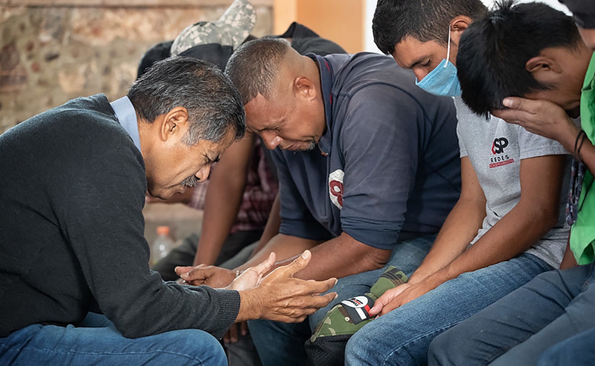 El Obispo Felipe Ruiz Aguilar (izquierda) de La Iglesia Metodista en México ora con los migrantes en el refugio Oasis en el Medio del Camino que la iglesia tiene en la localidad de Apaxco. Foto de Mike DuBose, Noticias MU.