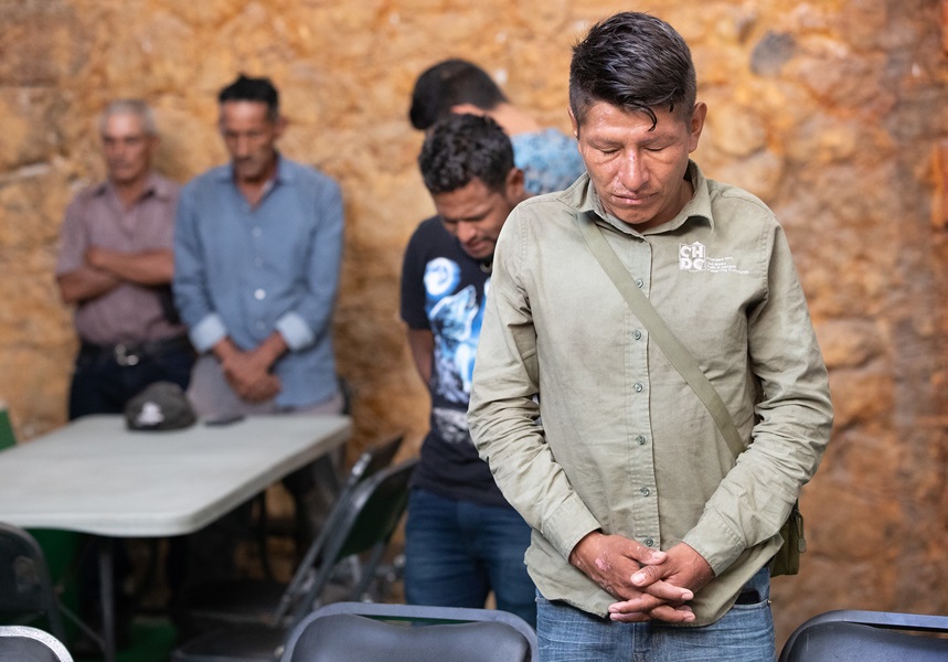Santos, un migrante de Honduras, se une a la oración con sus compañeros de viaje antes del desayuno en el refugio para migrantes Oasis en el Medio del Camino en Apaxco. Santos resultó herido recientemente cuando se cayó de “La Bestia”, el nombre con el que se conoce a la red de trenes de carga que muchos/as usan para viajar hacia la frontera norte de México. Foto de Mike DuBose, Noticias MU.