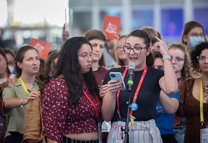 Dozens of young assembly participants gather during a business plenary session of the WCC 11th Assembly to demand better representation and to have their voices be heard more loudly in the worldwide fellowship of churches. At the microphone is Isabella Reimann Gnas of the Evangelical Lutheran Church of Brazil. Photo by Albin Hillert/WCC.