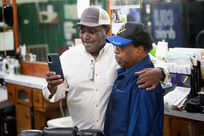 Nathan Marsh (left) shares a video with Jake Sherrell at the barbershop where they both work. “I’ve been with Jake for the last 35 or 40 years,” Marsh said. “He’s been a mentor to me. I love working with him. He’s a cousin. He’s a mentor. We love him. The whole neighborhood loves him.” Photo by Mike Dubose, UM News.