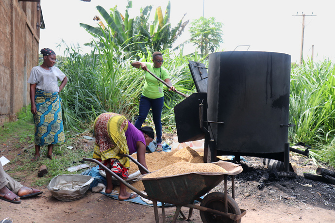 Elfreda Brima-Fawundu (right) from Sierra Leone helps remove boiled rice from a parboiled rice steamer at the Songhai Center. Attendees of the training program visited the rice-processing department to learn about the simple and affordable technology. Photo by Phileas Jusu, UM News.