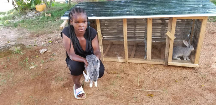 HAPIGro is a youth animal husbandry initiative that trains youth to raise and care for animals. As offspring are born, the youth "pass the gift" to other youth. Naïkenlove Antoine holds one of her rabbits in front of the hutch where the animals live. Photo courtesy of Valerie Mossman-Celestin, director of HAPI.