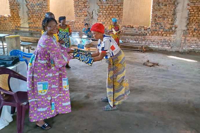Mathilde Onotamba, présidente des femmes (à gauche), remet une pièce de pagne à une veuve lors de la cérémonie de distribution à l’Église locale Méthodiste Unie de Kisangani. Pour permettre aux veuves de bien passer des fêtes de fin d’années, l’Association des Mamans Veuves, une branche de l’Agence des Femmes Méthodistes Unies de la Conférence Annuelle des Provinces Orientale et Équateur, a apporté une assistance en vivres et non-vivres à plus de 30 veuves. Photo Lebon Okito, UM News.