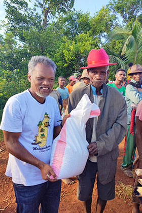 Bodo Abani Marielle (avec le chapeau rouge) reçoit des denrées alimentaires du pasteur Jean Aime Ratovohery de l’église Méthodiste Unie d’Ambodifasika lors d’un voyage missionnaire à Andranomavo, Madagascar. Les membres de l’église ont distribué de la nourriture aux familles touchées par le Cyclone Freddy, qui a dévasté la région au début de l’année. Photo de Justin Rakotoarimanana.
