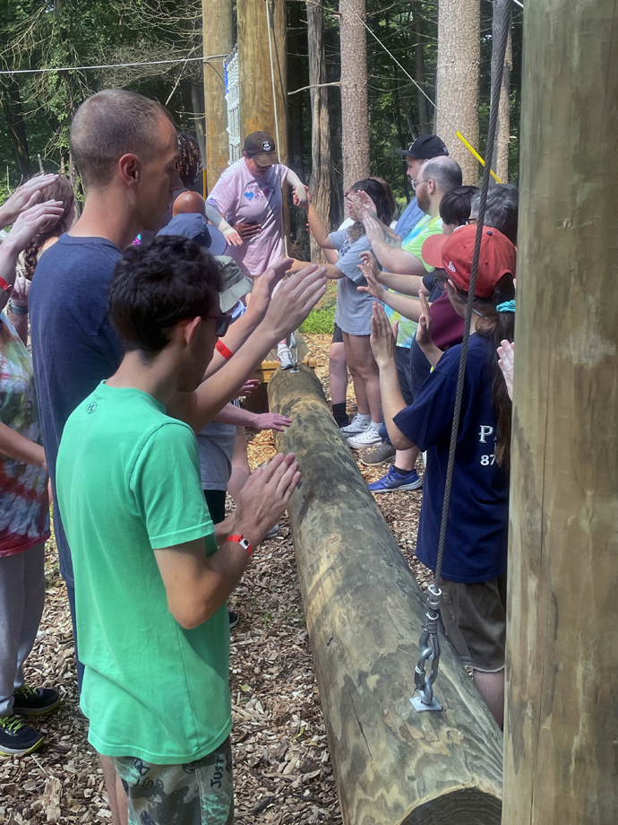 A camper tries to maintain balance while walking the length of a log at Innabah Camp and Retreat Center in Spring City, Pa., on June 29. Other campers line up along the route to help. The log is one of a series on the obstacle course. Photo by Jim Patterson, UM News.