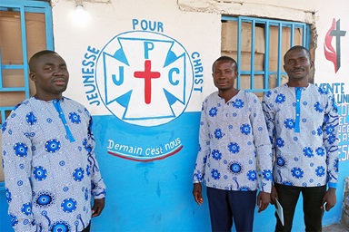 Des responsables actuels et anciens du comité des jeunes de la Kabondo Center United Methodist Church se tiennent devant la boutique de l'église qu'ils gèrent pour générer des revenus pour les jeunes de Kabondo, au Congo. William Ilunga Mushimukata, Ngulu Mingi et Hugo Banza Kyakulomba (de gauche à droite). Photo par la Révérende Betty Kazadi Musau, UM News. Des responsables actuels et anciens du comité des jeunes de la Kabondo Center United Methodist Church se tiennent devant la boutique de l'église qu'ils gèrent pour générer des revenus pour les jeunes de Kabondo, au Congo. William Ilunga Mushimukata, Ngulu Mingi et Hugo Banza Kyakulomba (de gauche à droite). Photo par la Révérende Betty Kazadi Musau, UM News.