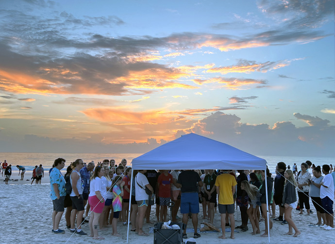 Docenas se reúnen bajo una carpa para comulgar al amanecer durante Juventud 2023 que se llevó a cabo en Daytona Beach, Florida del 25 al 28 de julio. Representantes de 12 de las 13 agencias de La IMU participaron como oradores/as, líderes de talleres y expositores/as. Foto de Crystal Caviness, Comunicaciones Metodistas Unidas. 