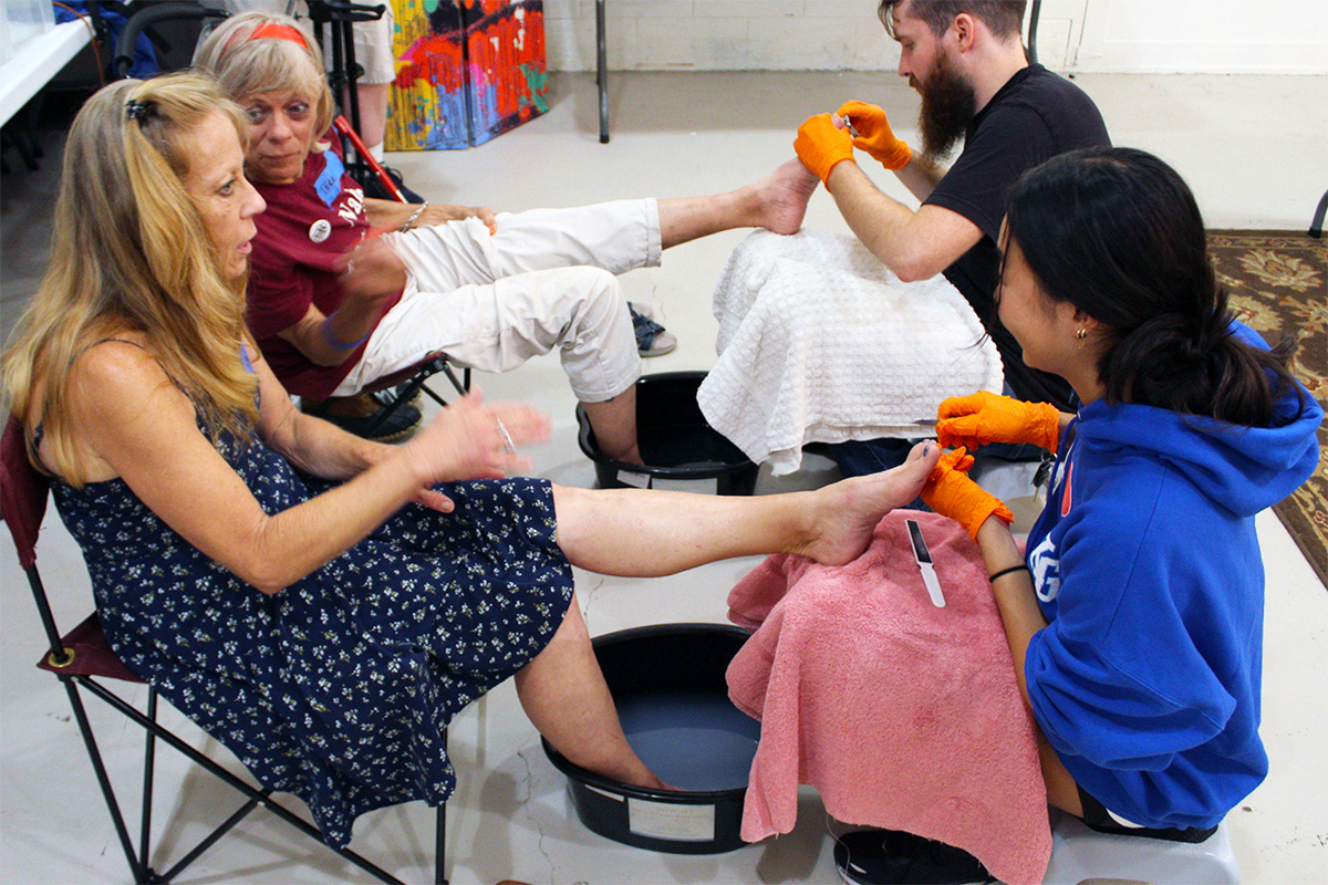 Will Compton, resource specialist for Open Table Nashville, and Jenna Lee, a volunteer, tend to Tanya (left) and Terri at a foot clinic service offered after a weekly Tuesday evening supper at Trinity Community Commons in East Nashville, Tennessee. Photo by Vernon Jordan, UM News.