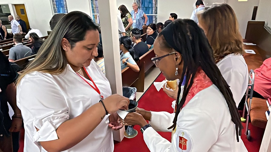 La Obispa Kennetha Bigham Tsai (derecha) ministra la comunión a la Paola Lemus Bustillos, pastora de la Conferencia Anual de Florida. Foto Rev. Gustavo Vasquez, Noticias MU.