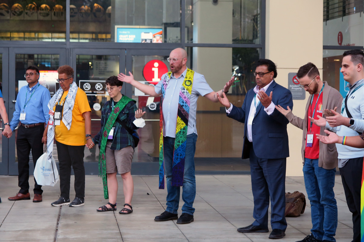 United Methodist clergy and lay members pray outside the Charlotte Convention Center in Charlotte, N.C., on Oct. 13  for the General Conference that will take place in its halls in about six months. The United Methodist Queer Clergy Caucus organized the prayer session for the denomination’s top lawmaking assembly during the Reconciling Ministries Network Convocation in Charlotte. The Rev. Austin Adkinson, pastor of Light of the Hill United Methodist Church in Puyallup, Wash., leads the prayer. Photo by Heather Hahn, UM News.