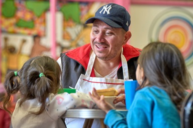 Víctor Lugo, un migrante venezolano habla con dos de sus nietas en CAFEMIN, un refugio para migrantes en la Ciudad de México. Fundado por las Hermanas Josefinas, una orden religiosa católica, el refugio se ha visto desbordado en los últimos meses por solicitudes de alojamiento y otras formas de asistencia. Lugo, que trabaja como voluntario en la cocina del refugio, viaja con siete miembros de su familia, incluidas las dos niñas. Están esperando una cita con funcionarios/as de inmigración mexicana, con la esperanza de obtener una visa de tránsito que les permita avanzar más al norte. Foto del Rev. Paul Jeffrey, Noticias MU. Víctor Lugo, un migrante venezolano habla con dos de sus nietas en CAFEMIN, un refugio para migrantes en la Ciudad de México. Fundado por las Hermanas Josefinas, una orden religiosa católica, el refugio se ha visto desbordado en los últimos meses por solicitudes de alojamiento y otras formas de asistencia. Lugo, que trabaja como voluntario en la cocina del refugio, viaja con siete miembros de su familia, incluidas las dos niñas. Están esperando una cita con funcionarios/as de inmigración mexicana, con la esperanza de obtener una visa de tránsito que les permita avanzar más al norte. Foto del Rev. Paul Jeffrey, Noticias MU.