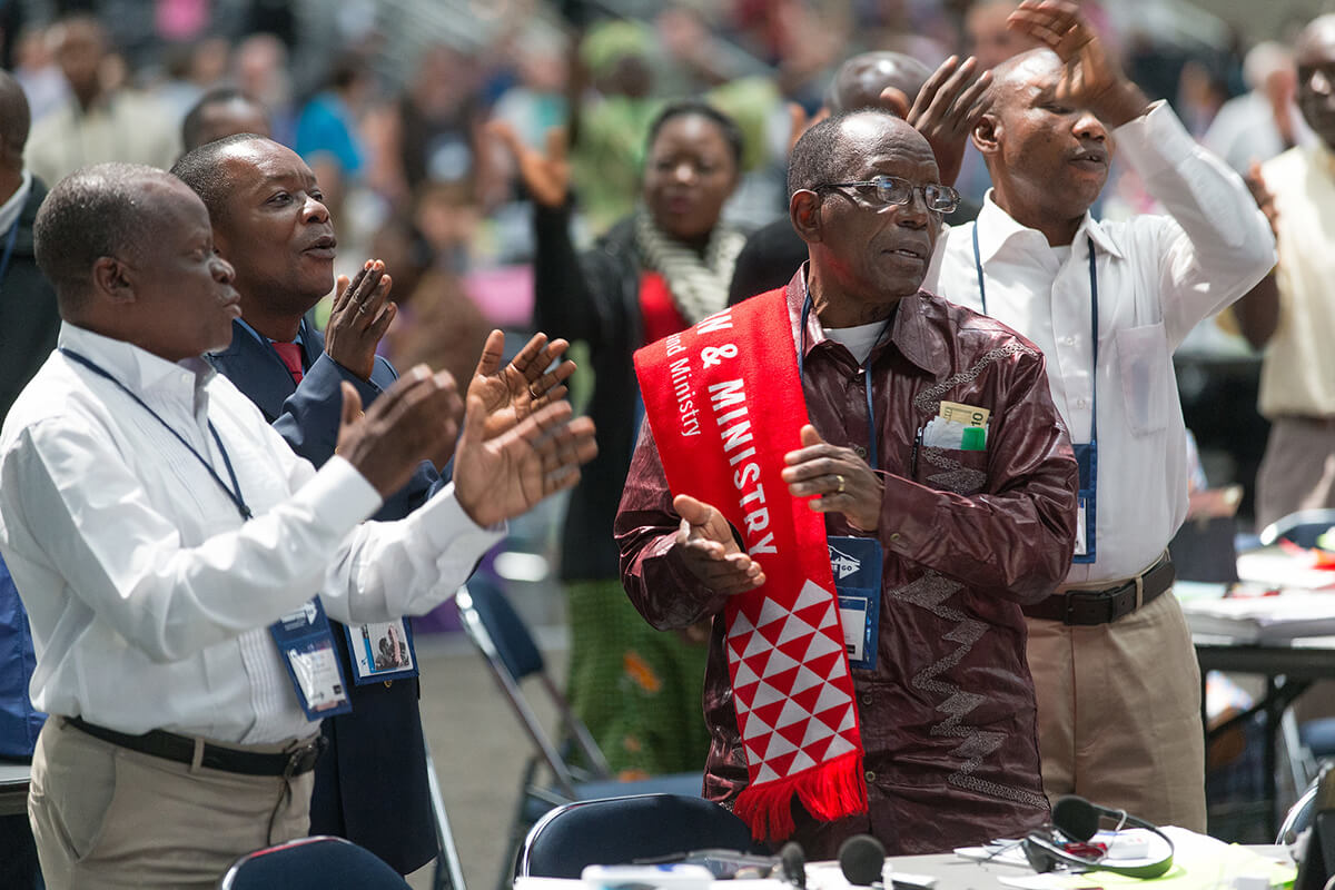 Michel Lodi da Conferência do Leste do Congo (primeiro plano à direita) junta-se a outros delegados Africanos cantando durante um intervalo na Conferência Geral Metodista Unida de 2016 em Portland, Oregon. Os líderes da Igreja dizem que os problemas de visto estão a causar uma dificuldade para conseguir delegados de fora dos EUA à Conferência Geral que começa a 23 de Abril em Charlotte, N.C. Os grupos Metodistas Unidos Africanos alertam que a sua região pode estar significativamente sub-representada. Foto de arquivo de Mike DuBose, Noticias da MU.