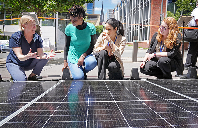The Rev. Jenny Phillips, director of environmental sustainability with the United Methodist Board of Global Ministries, talks with Shamiso Apart, Ilka Vega and Megan Hale about the Mobile Solar Power Station on display at the United Methodist General Conference in Charlotte, N.C., on May 1. Photo by Larry McCormack, UM News.