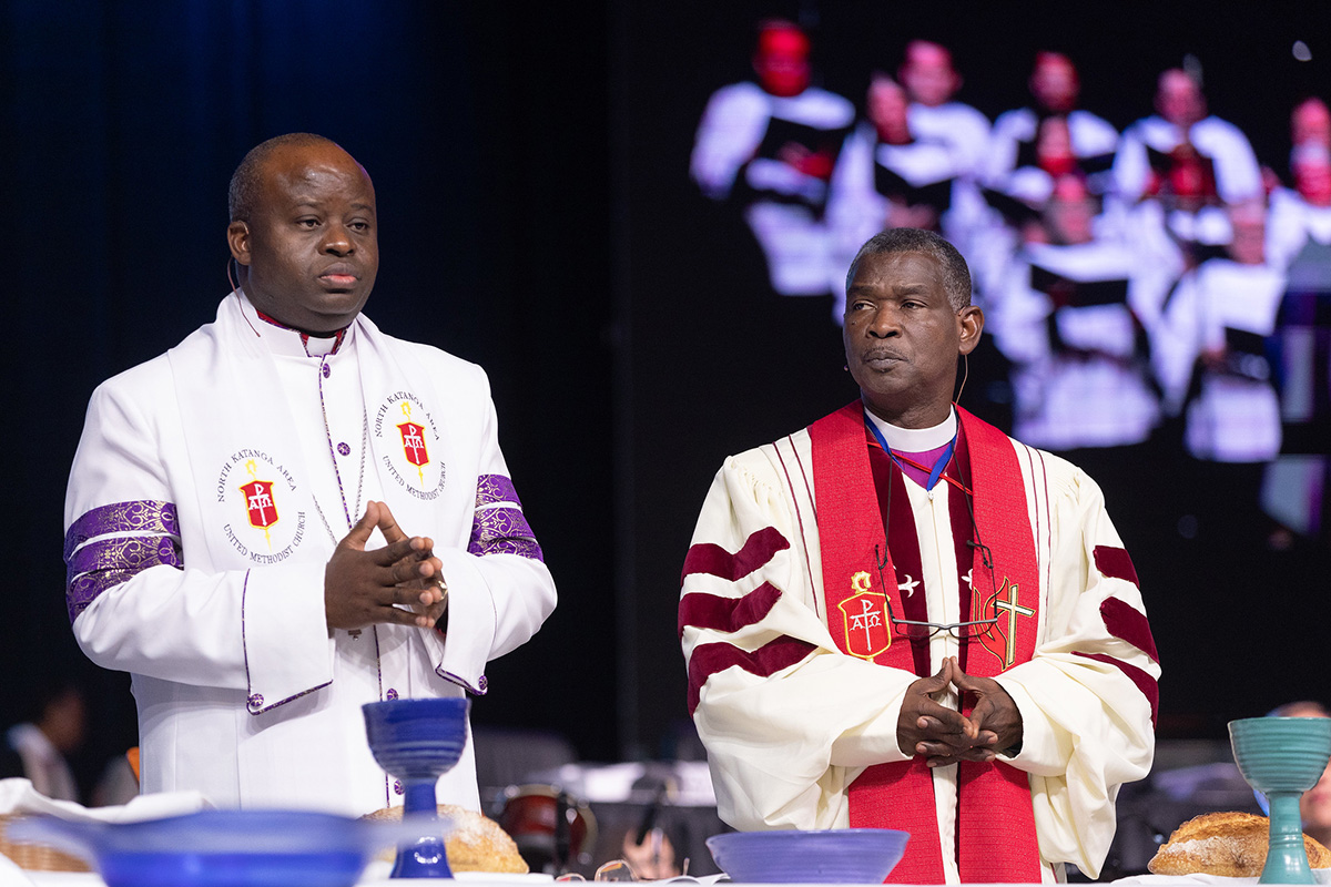 Maaskofu Askofu Mande Muyombo (gauche) wa Conférence ya Nord Katanga na Gaspar João Domingos wa Conférence ya Angola wanabariki Sainte Cène wakati wa ibada ya ufunguzi wa 23 avril katika Conférence Générale ya Église Méthodiste Unie huko Charlotte, Caroline du Nord. Picha na Mike DuBose, UM News.