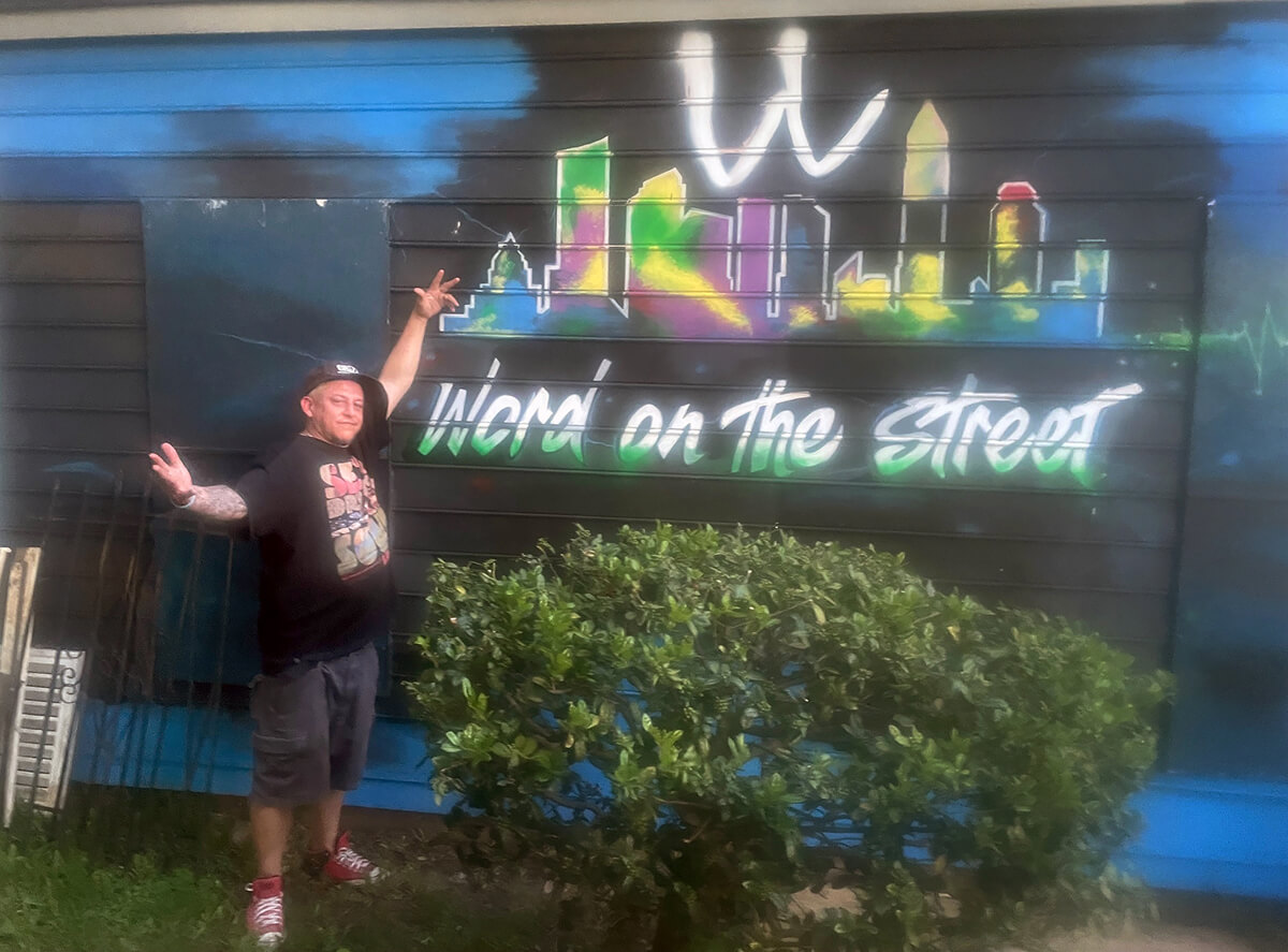 Artist Manny Blanco shows off a mural on April 30 that he painted on the outside wall of Hope Chapel, a ministry in Charlotte, N.C., that offers meals and other support to the homeless in that city. Photo by Jim Patterson, UM News.