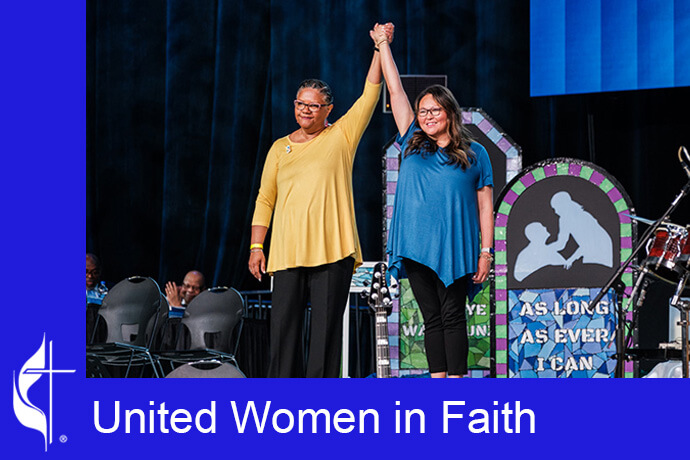 Sally Vonner, United Women in Faith top executive, and Bethany Amey Sutton, secretary of the group’s Executive Board, join hands on stage at the United Methodist General Conference in Charlotte, N.C., on April 29. Photo by Corbin Payne.