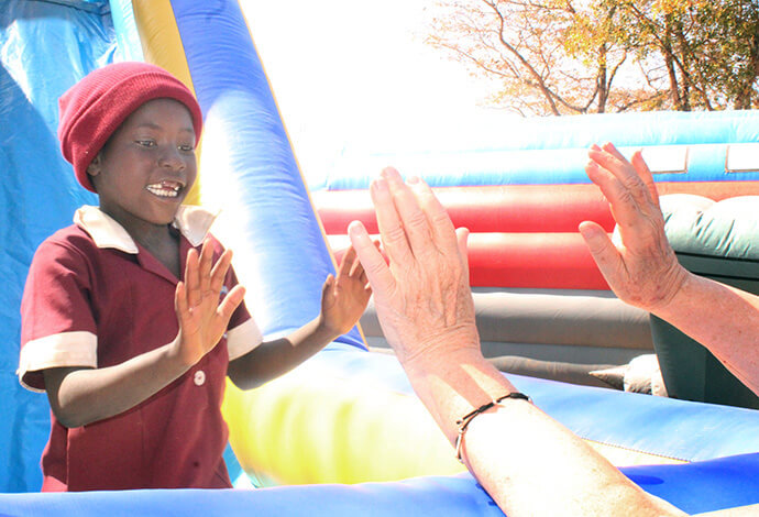 First-grader Mavis Turuside slaps hands with volunteer Barbara Julian at the bottom of a slide. Photo by Kudzai Chingwe, UM News.