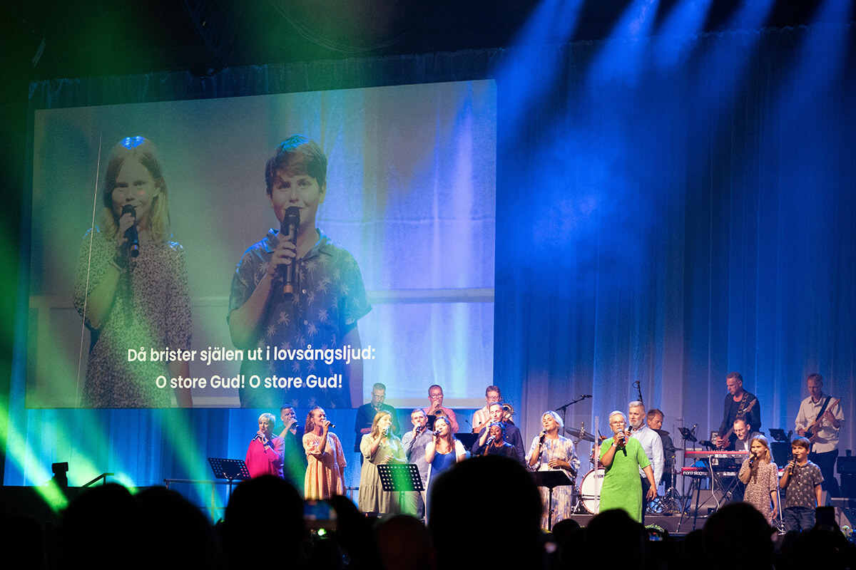 Os irmãos Agnes e Alfred Quint (na tela) se juntam aos cantores da Uniting Church na Suécia para liderar os adoradores em “O Store Gud”, o nome sueco original do hino que os falantes de inglês conhecem como “How Great Thou Art”, durante a World Methodist Conference em Gotemburgo, Suécia. Foto de Klaus Ulrich Ruof, Germany Central Conference.