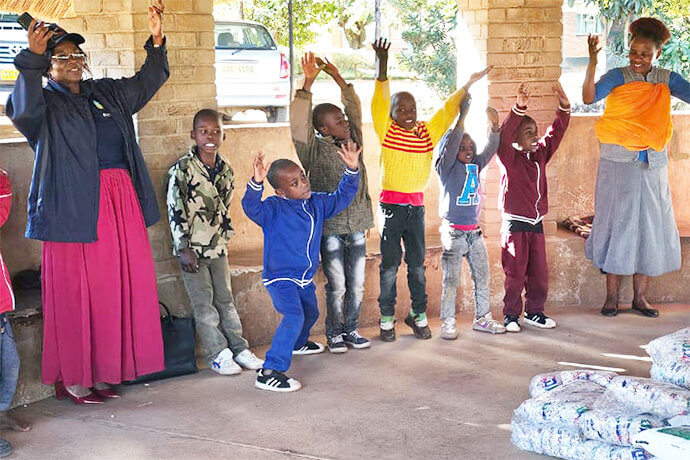 Florence Kachingwe (à gauche, en jupe rose), présidente de la Class of 81 Charitable Foundation, chante et danse avec les enfants du Fairfield Children's Home, un foyer pour enfants affilié à l'Église Méthodiste Unie à Mutare, au Zimbabwe. La fondation, créée par d'anciens élèves du Lycée Méthodiste Uni Hartzell, a fait don de nourriture et d'autres fournitures à l'école. Photo de Tafadzwa Gumbochuma.