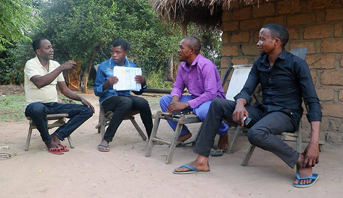 Michel Tahindja Tashinga (from left) and Kitete Kahodi, United Methodist community relays based in the villages of Wenga and Dikungu, respectively, talk with Patrice Lumumba Okeke (in purple) and another resident about mpox. “Thanks to the information given, I can recognize the symptoms and know what to do if I notice them in myself or someone else in my family,” said Okeke, who leads a family of eight. Photo by Chadrack Tambwe Londe, UM News.