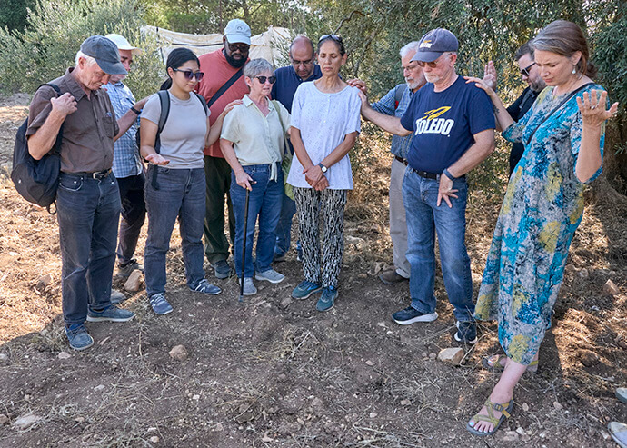 The Rev. Larry Clark, a United Methodist pastor from Toledo, Ohio (in blue Toledo shirt), joins with other members of a delegation of church activists from the United States to pray over Amal Nassar (center), who helps run a family farm near Bethlehem that sits on the last remaining Palestinian hilltop in the middle of the Gush Etzion settlement block in the occupied West Bank. The Christian Palestinian family remains under constant threat from settlers and the Israeli military. Photo by Paul Jeffrey, UM News.