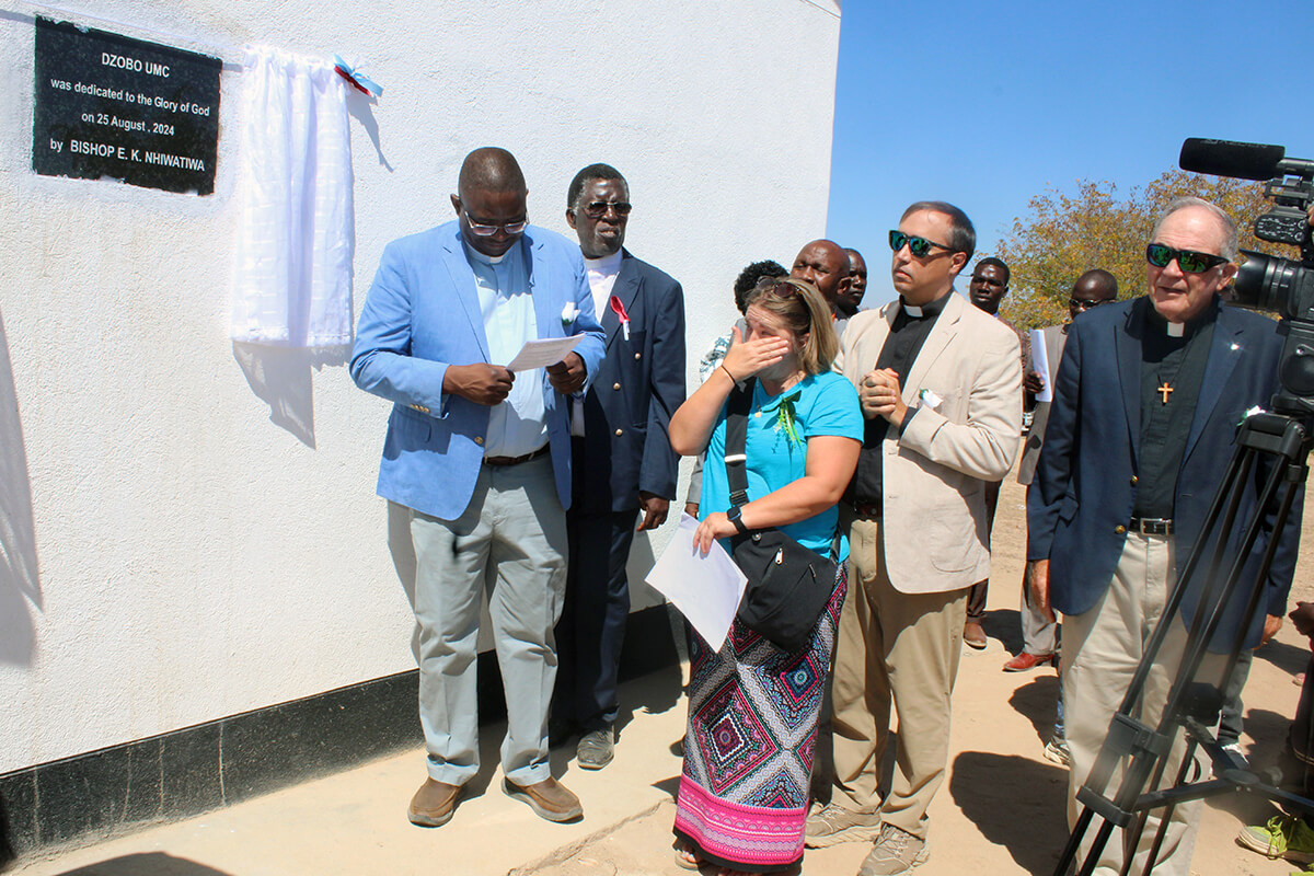 Amy Carmon, membre de l'Église Méthodiste Unie Mary's Chapel à Bean Station (Tennessee), est émue lors de la cérémonie d'inauguration de l'Église Méthodiste Unie Dzobo dans la campagne zimbabwéenne. À gauche, le révérend Samuel Dzobo, dont le rêve d'un sanctuaire dans son village natal a incité Mary's Chapel à collecter 48 000 dollars pour aider à la construction de l'église. À droite, le révérend Gerald Russell, pasteur retraité de la Conférence Holston et ancien missionnaire méthodiste uni. Photo par Kudzai Chingwe, UM News.