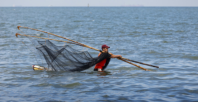 A fisherman searches the shallow waters for small fish just off the beach in the Mozon II neighborhood in Rosario. The customary fishing grounds in deeper water were closed by the government due to oil spills during Typhoon Carina. Photo by Mike DuBose, UM News.