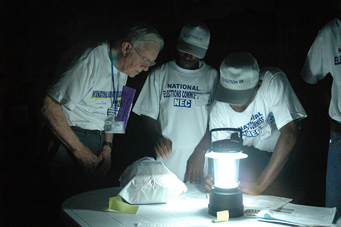 Jimmy Carter assiste au dépouillement des bulletins de vote à la lumière d'une lampe dans un bureau de vote au Libéria lors de l'observation des élections présidentielles par le Centre Carter le 11 octobre 2005. Photo avec l'aimable autorisation du Centre Carter.