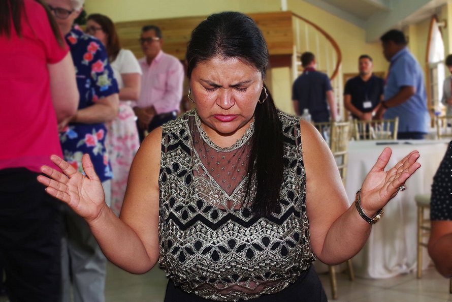 La hna. Arely Rodríguez, delegada laica a la reunión anual, ora de rodillas en el altar después de recibir los elemento durante la eucaristía celebrada en el culto inaugural.