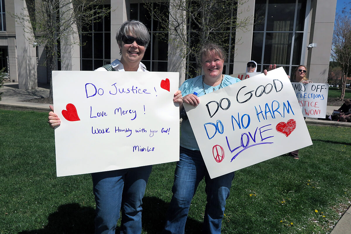Cheryl Lowe (left) and Andrea Gauldin-Rubio, both United Methodists, hold their signs based on Scripture and the teachings of John Wesley at the Hands Off! rally on April 5 outside the courthouse in Waynesville, North Carolina. They were among many United Methodists who used their lunchtime during the nearby Peace Conference to attend the nonviolent rally decrying government overreach. Lowe is a member of Mt. Pleasant United Methodist in McLeansville, N.C., and Gauldin-Rubio is the director of Christian education at Bunker Hill United Methodist Church in Kernersville, N.C. Photo by Heather Hahn, UM News.