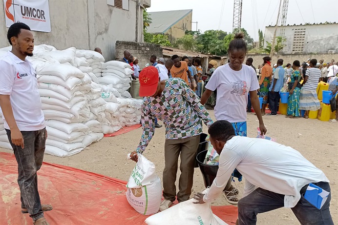 Des bénéficiaires prennent des sacs de riz et de farine de maïs, tandis qu'un volontaire se tient debout lors d'une opération de distribution de nourriture à Kisangani. Grâce à un financement de 150 000 dollars de UMCOR (United Methodist Committee on Relief), l'Église Méthodiste Unie a aidé plus de 10 000 personnes déplacées, soit 1 600 ménages, dans la région de Kisangani. Photo par Lebon Okito, UM News. Des bénéficiaires prennent des sacs de riz et de farine de maïs, tandis qu'un volontaire se tient debout lors d'une opération de distribution de nourriture à Kisangani. Grâce à un financement de 150 000 dollars de UMCOR (United Methodist Committee on Relief), l'Église Méthodiste Unie a aidé plus de 10 000 personnes déplacées, soit 1 600 ménages, dans la région de Kisangani. Photo par Lebon Okito, UM News.