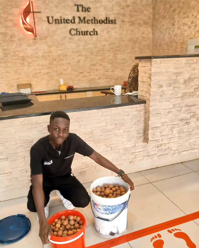 Africa University graduate Panashe Banda displays buckets of mazhanje, an African wild fruit, he brought as a gift to the Zimbabwe West Conference head office staff. Banda has been sharing his family’s harvest with the staff each year as a thank you for the church scholarship he received to attend the United Methodist university in Mutare, Zimbabwe. Photo by Chenayi Kumuterera, UM News.