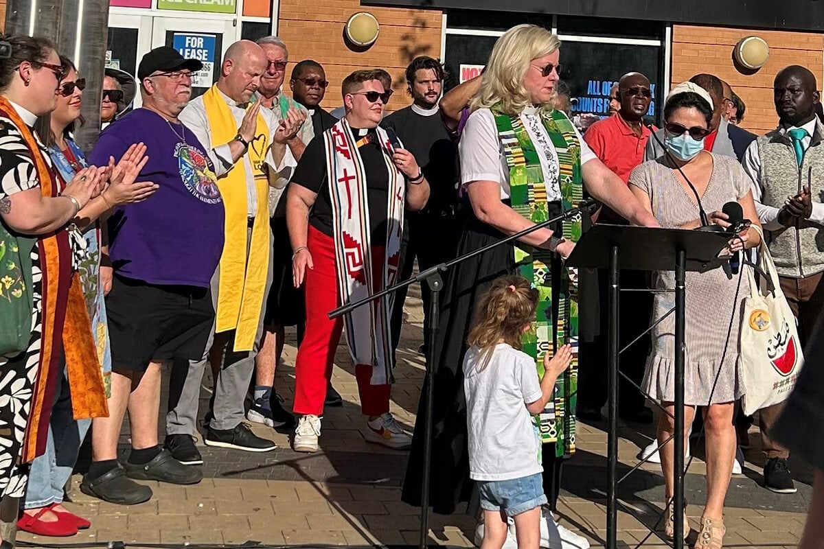 Cerca de 40 líderes religiosos de Washington, D.C., se unem em 22 de agosto para liderar uma vigília de oração no bairro etnicamente diverso de Columbia Heights. O grupo teve como objetivo apresentar uma visão de unidade e esperança diante do envio de tropas da Guarda Nacional por Trump para a capital do país. No centro, com a estola verde e branca, está a Revda. Donna Claycomb Sokol, pastora da Igreja Metodista Unida de Mount Vernon Place, que discursou no evento. Foto de Sharon Groves, do Festival Center.