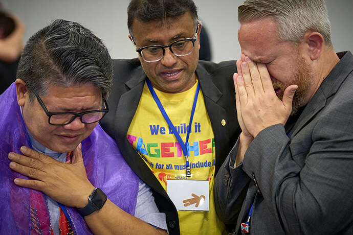 The Revs. Izzy Alvaran (left), Scort Christy and Andy Oliver weep and pray together after the 2024 United Methodist General Conference, meeting in Charlotte, N.C., voted to remove the denomination's ban on the ordination of clergy who are "self-avowed practicing homosexuals" — a prohibition that dated to 1984. Oliver, pastor at Allendale United Methodist Church in St. Petersburg, Fla., is committed to activism in his community and said he feels called to ministry with people on the margins. File photo by Paul Jeffrey, UM News.