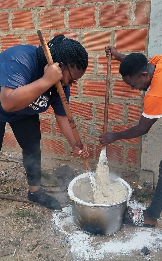 Tapiwanashe Moreblessing Manyeza (left) and a young man cook cassava pap, a common dish in Angola, to share during lunch in the Mucondo-Bengo Province. Manyeza visited the community in June of 2024 to assess its needs for clean water. Photo courtesy of Tapiwanashe Moreblessing Manyeza.